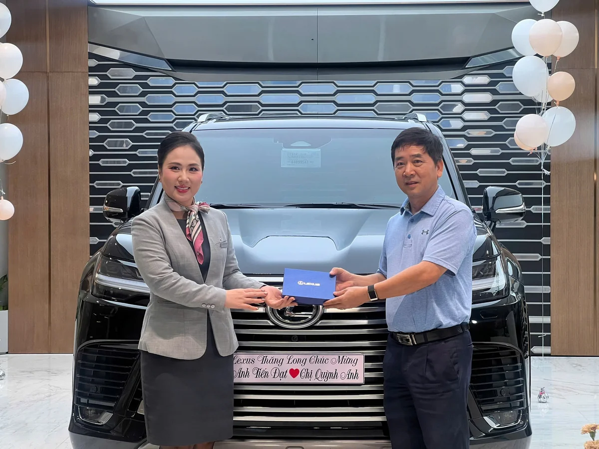 Chuyên viên và khách hàng cùng cầm hộp bàn giao trước xe Lexus
